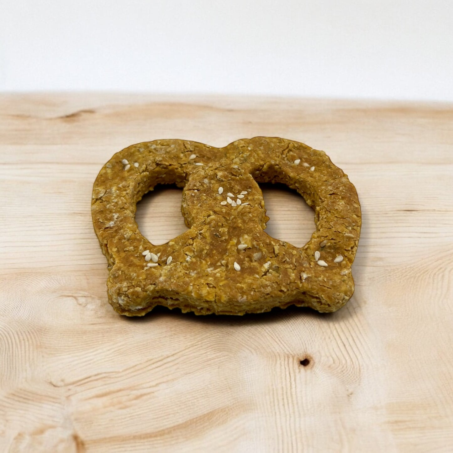 A pretzel-shaped dog treat made with cheddar cheese, placed on a wooden surface.