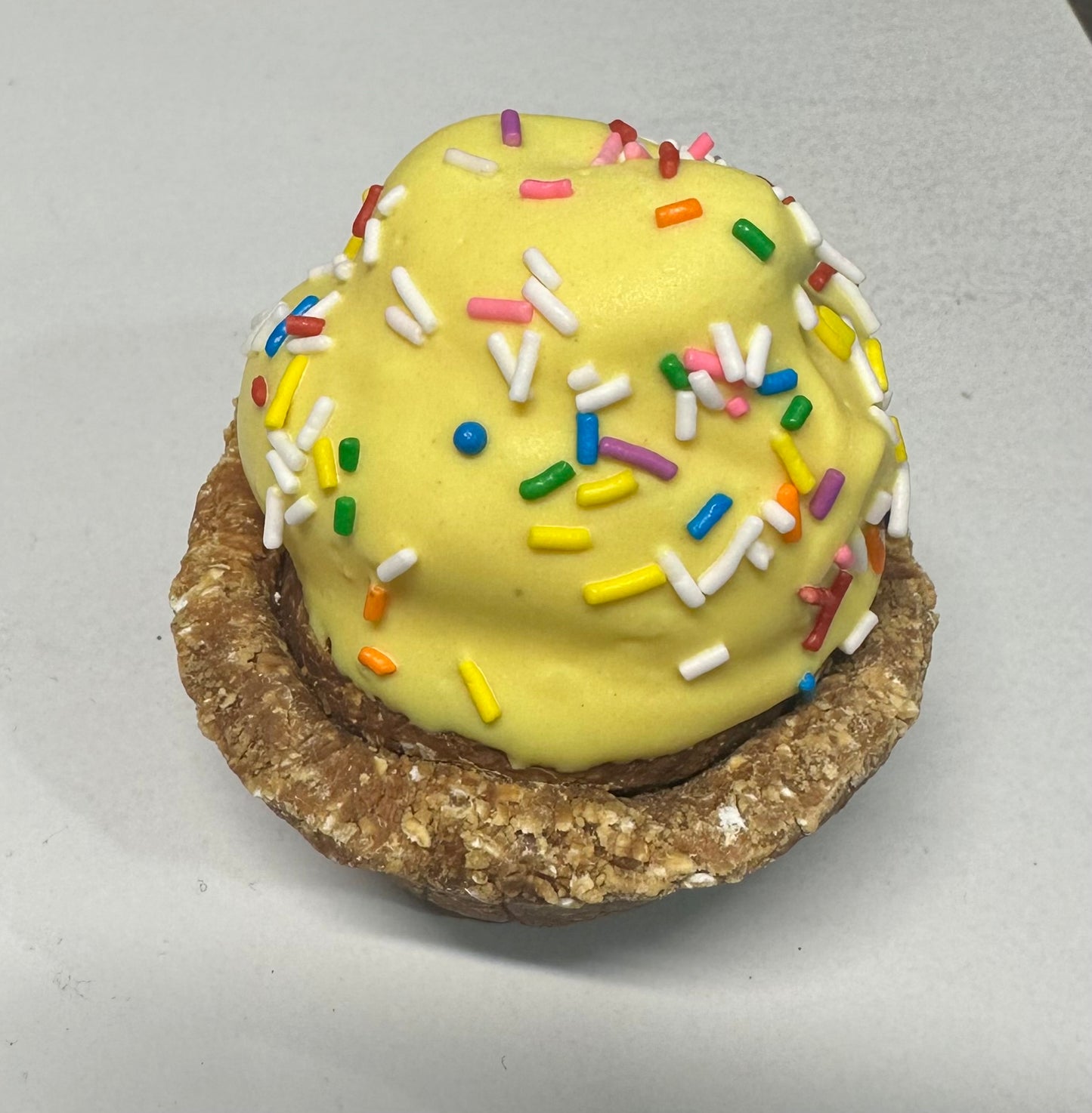 Yellow dog cupcake with sprinkles on a wooden surface.