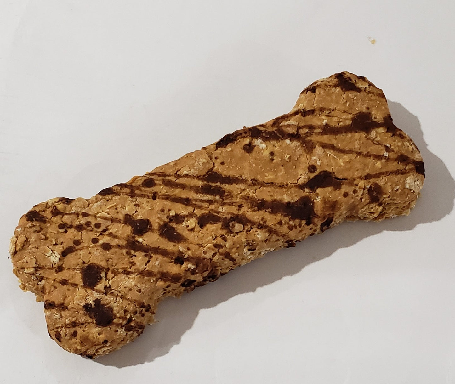 A bone-shaped dog treat with peanut butter and carob drizzled on top, placed on a wooden surface.