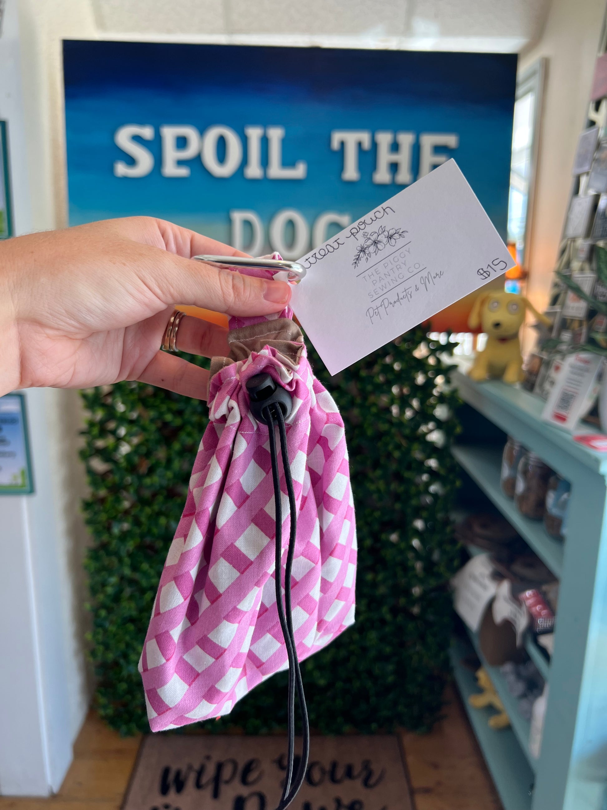 Hand holding a pink and white checkered bag with a tag in front of a store shelf.