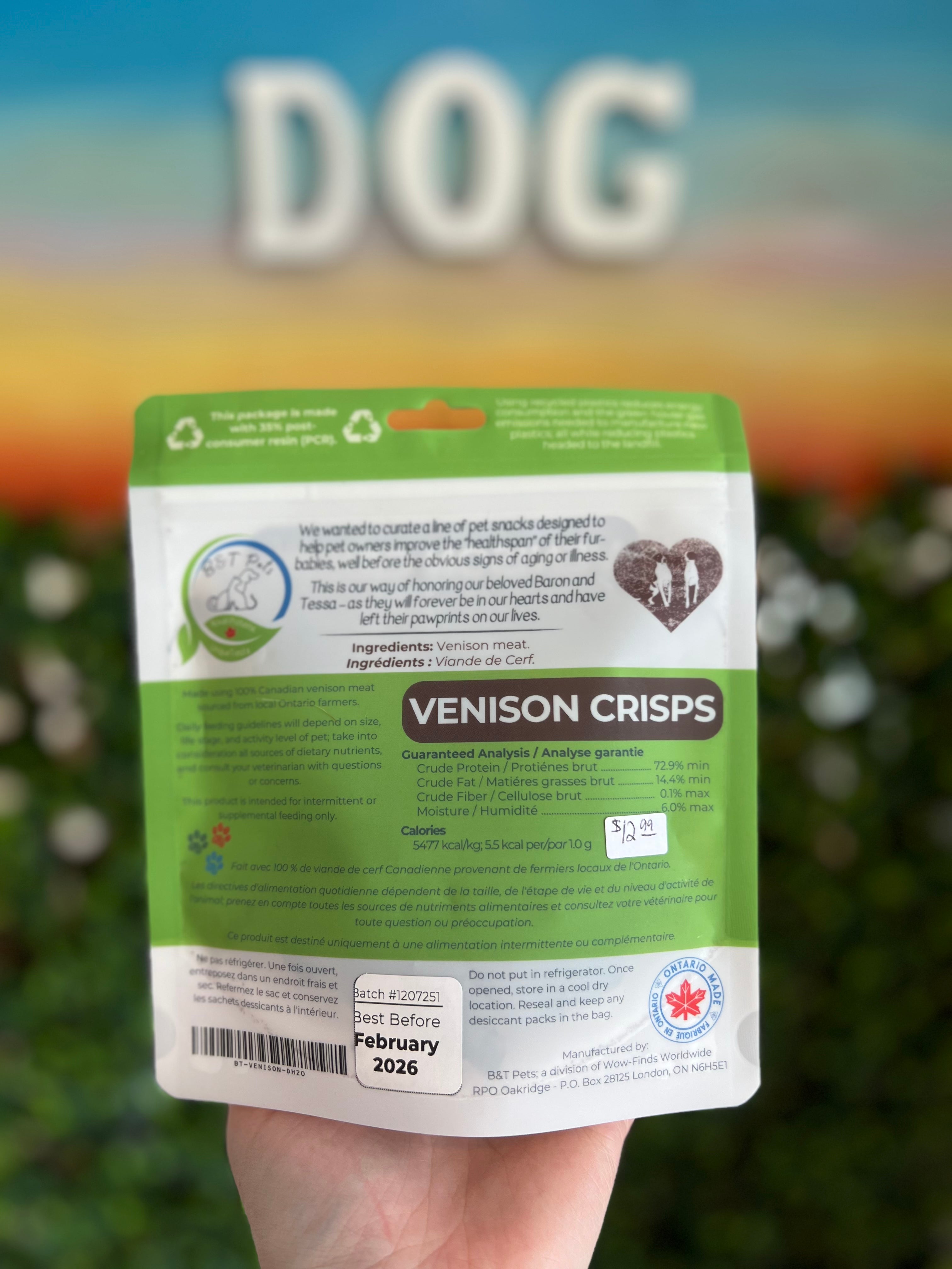 Hand holding a package of Venison Crisps for dogs with a blurred outdoor background