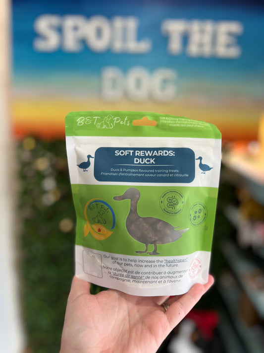 Hand holding a package of 'Spoil the Dog' soft rewards with a blurred background.