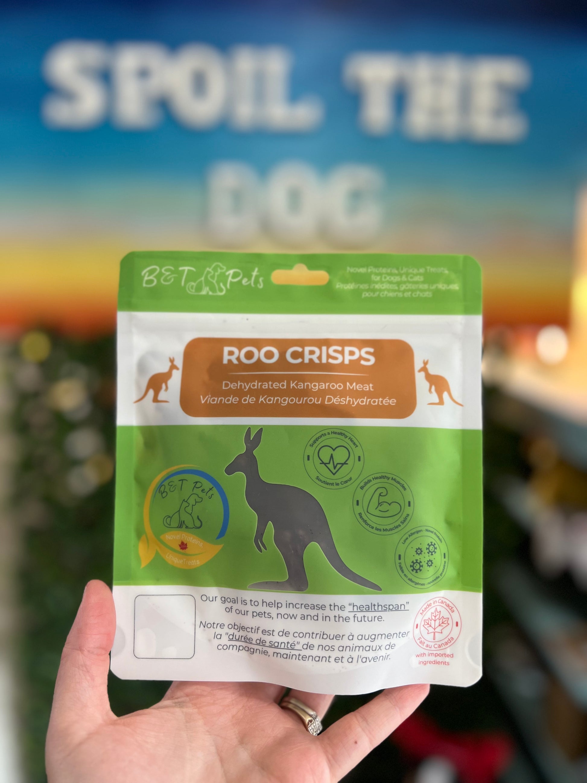 Hand holding a package of 'Roo Crisps' dehydrated kangaroo meat for dogs with a blurred background.