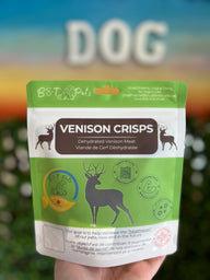 Bag of Venison Crisps for dogs held in front of a blurred background with 'DOG' text.