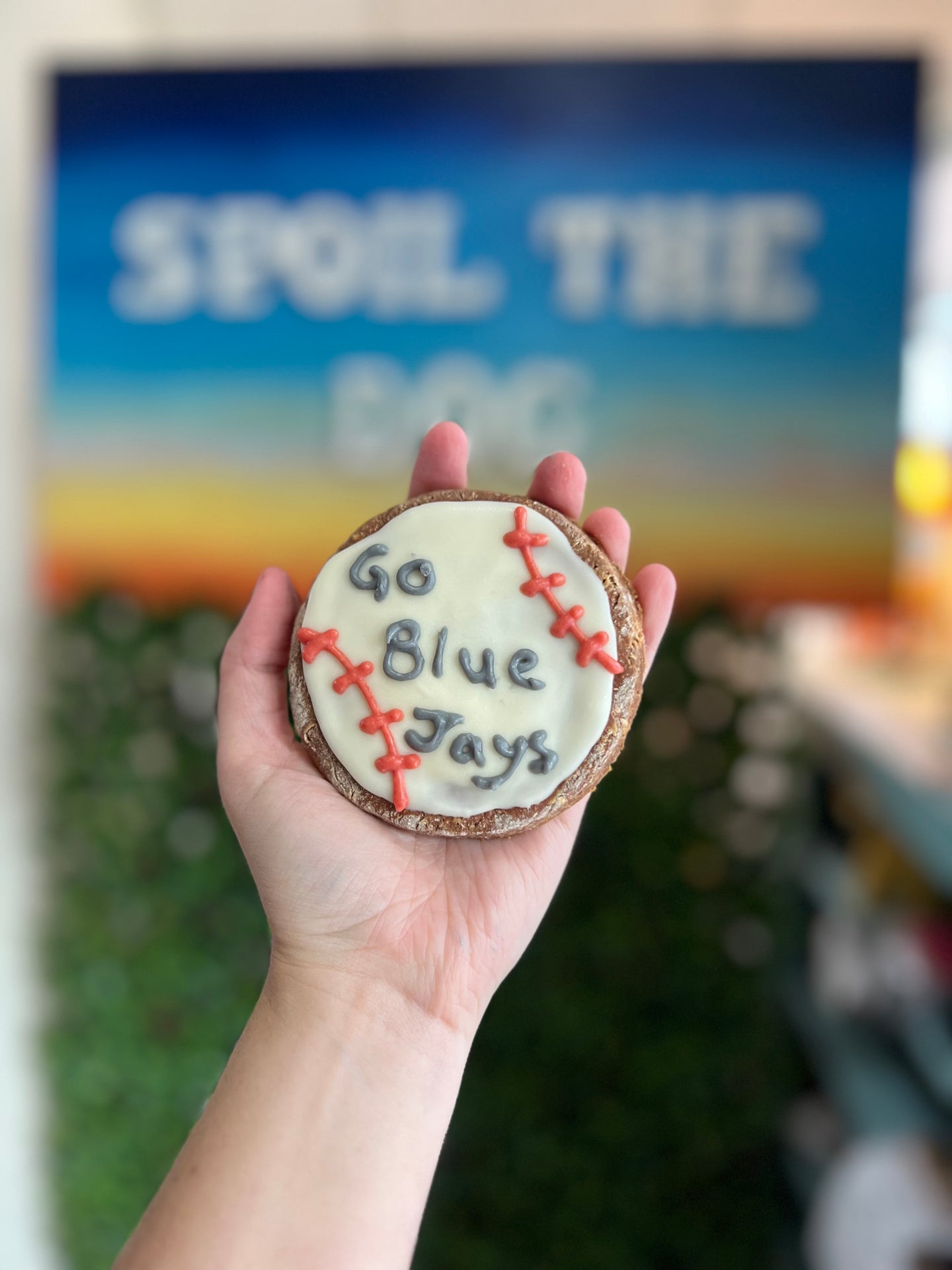 Hand holding a baseball cookie with 'Go Blue Jays' text against a blurred  background