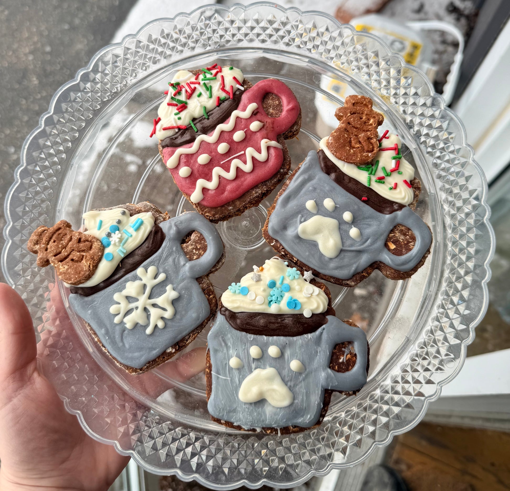 Decorative cookies shaped like mugs with snowflakes and paw designs, on a clear glass plate.