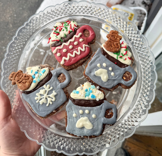 Decorative cookies shaped like mugs with snowflakes and paw designs, on a clear glass plate.