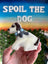 Hand holding a dog-shaped cookie with 'Spoil the Dog' branding in the background.