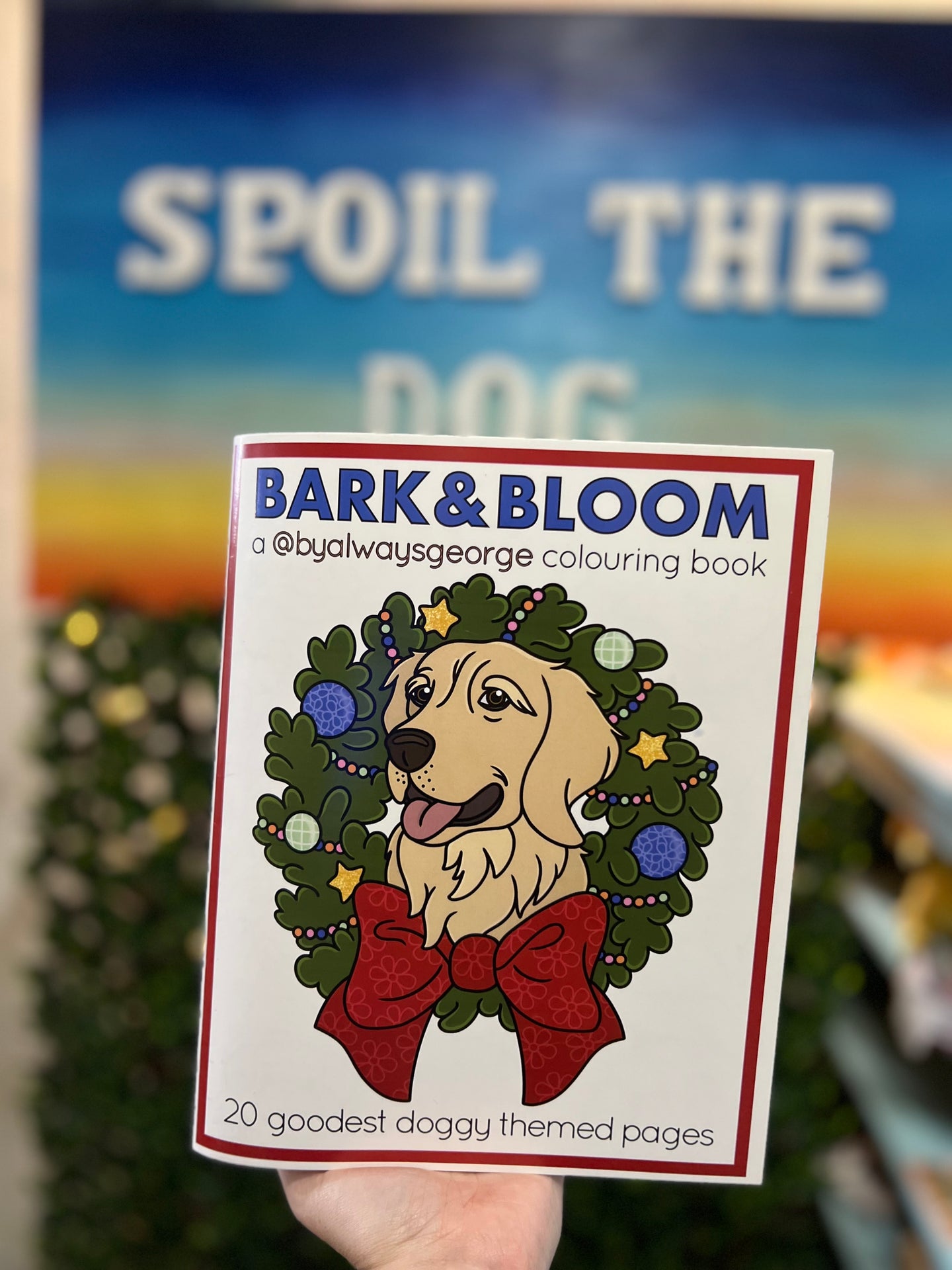 Bark & Bloom dog theme colouring book for children held in front of a blurred background with 'Spoil the Dog' text.