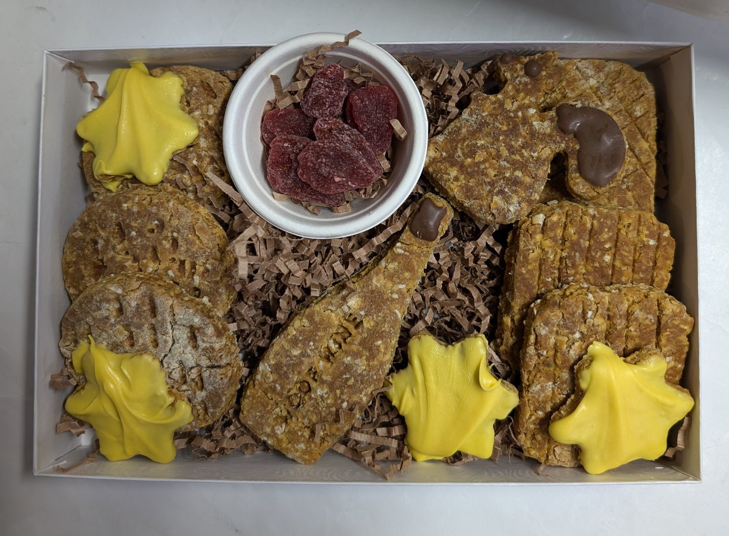 A dog treat Barkcuterie Box containing assorted natural dog treats arranged in an open box. Includes various natural dog treats such as 'crackers', 'cheese' diamonds, freeze dried strawberries and a squirrel shaped treat.