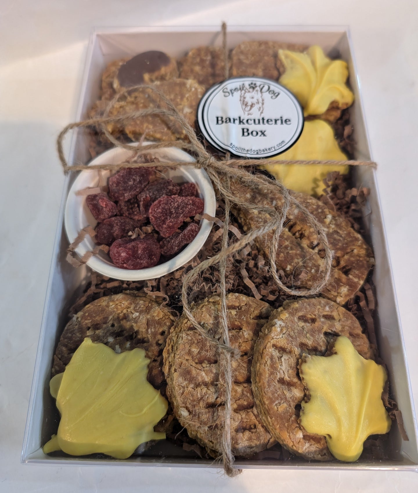 A dog treat Barkcuterie Box containing assorted natural dog treats arranged in a box, tied with a string and topped with a label.
