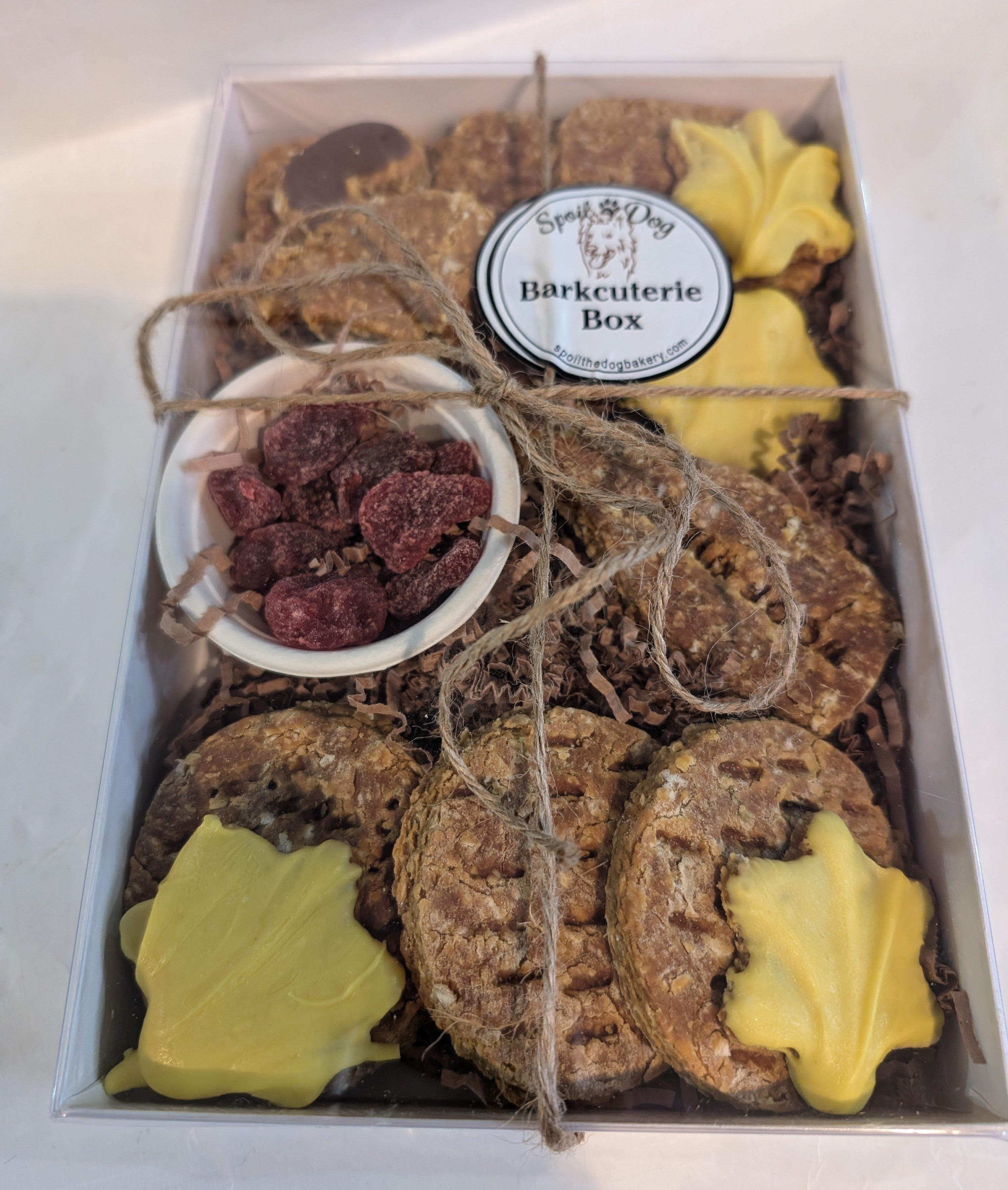 A dog treat Barkcuterie Box containing assorted natural dog treats arranged in a box, tied with a string and topped with a label.
