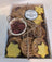 A dog treat Barkcuterie Box containing assorted natural dog treats arranged in a box, tied with a string and topped with a label.