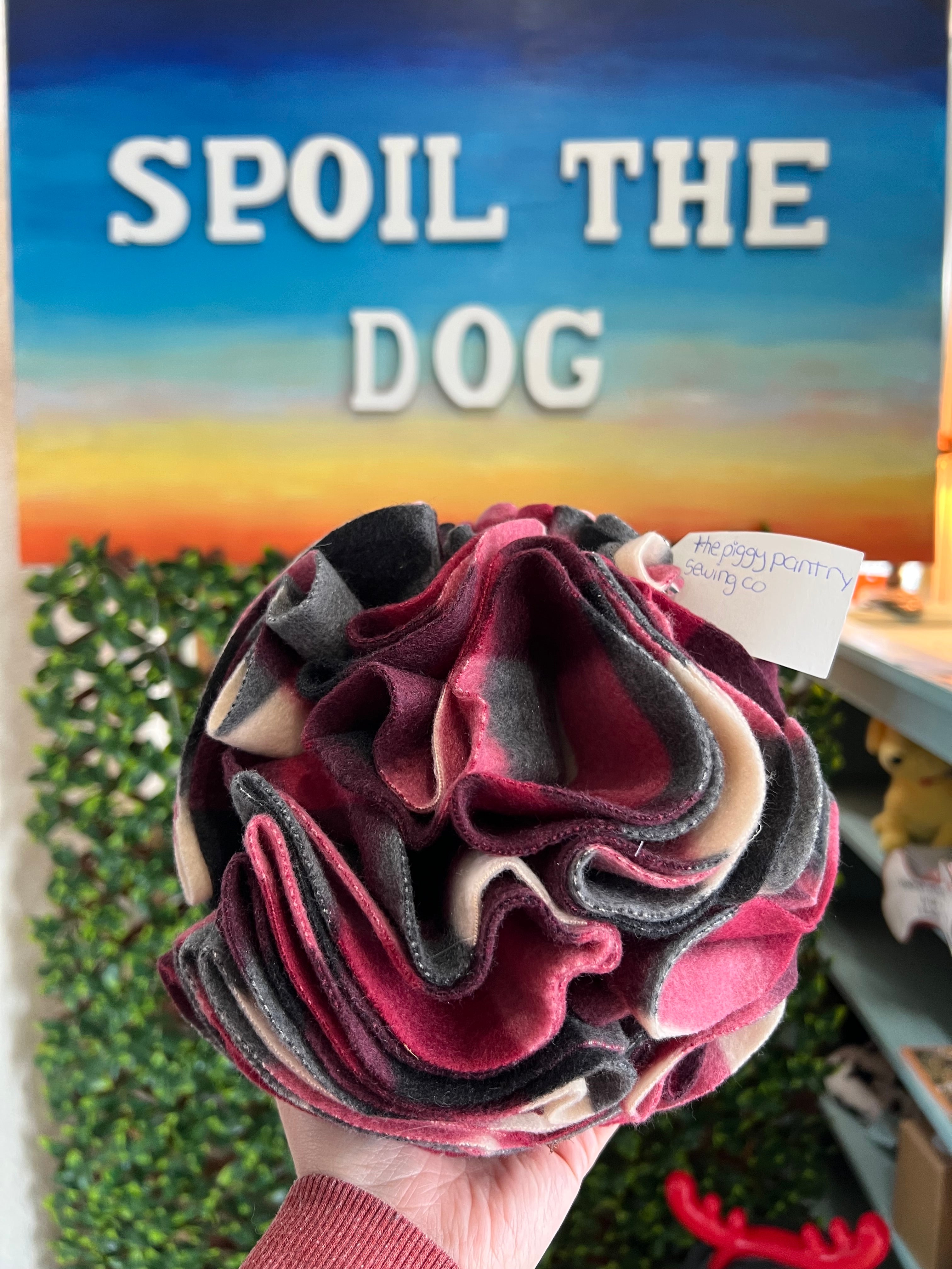 Snuffle ball held by a hand with 'Spoil the Dog' sign in the background