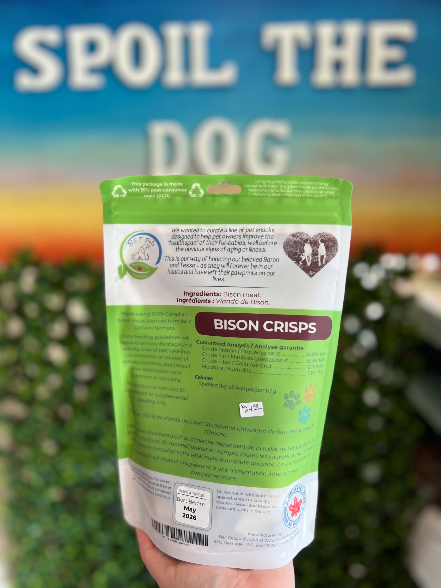Hand holding a package of 'Bison Crisps' with a blurred background featuring text 'SPOIL THE DOG'.