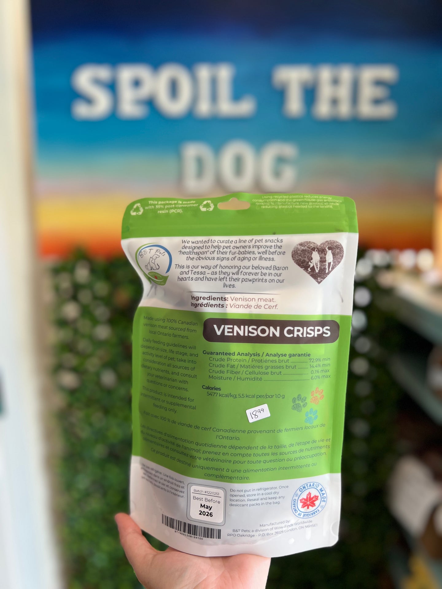 Hand holding a package of 'Venison Crisps' dog food with a blurred outdoor background.