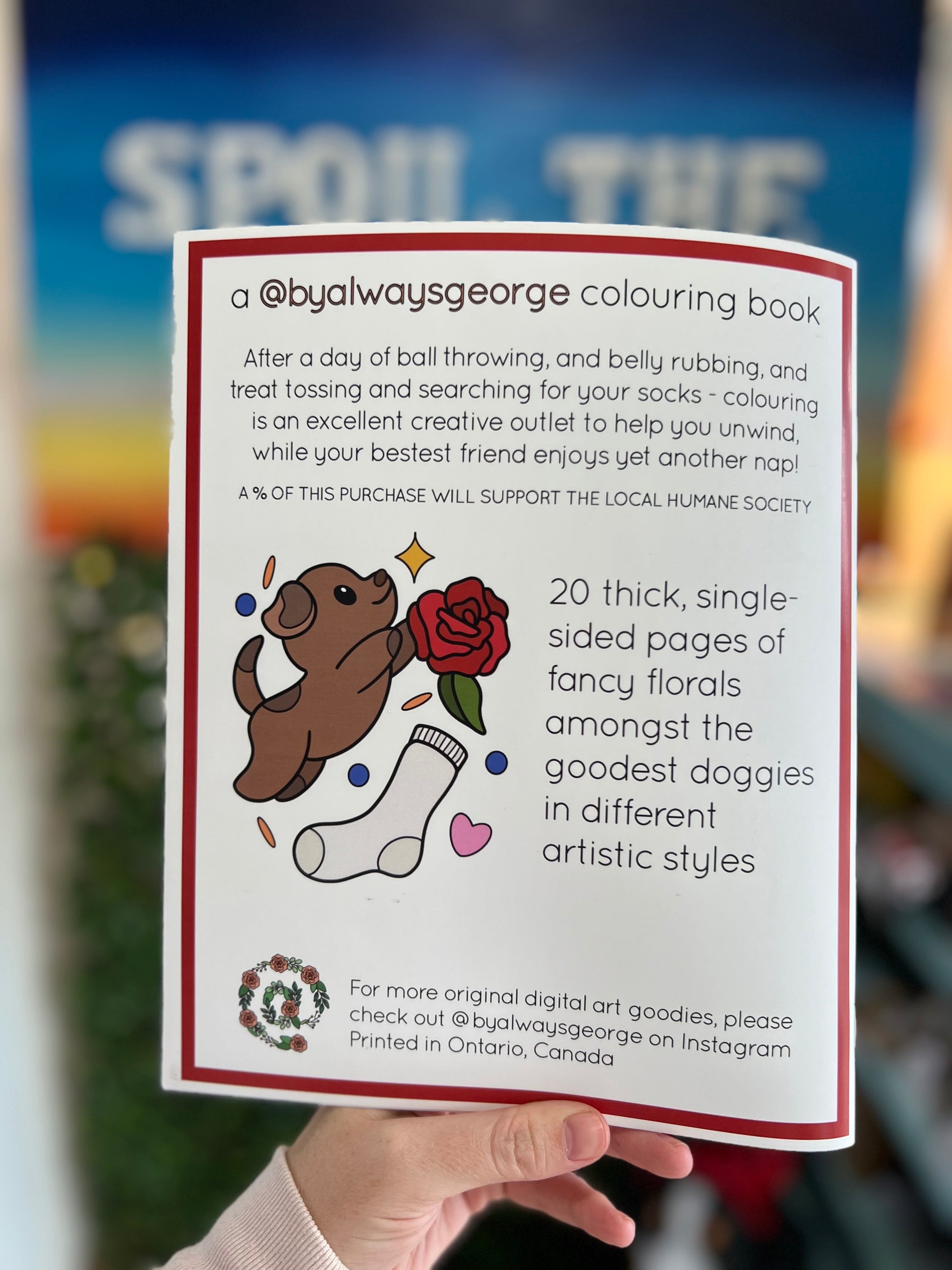 Coloring book with a dog and sock illustration held by a hand, against a blurred background.