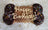 A jumbo bone-shaped dog treat with 'Happy Barkday' text and sprinkles on the bone's top edge, placed on a wooden surface.