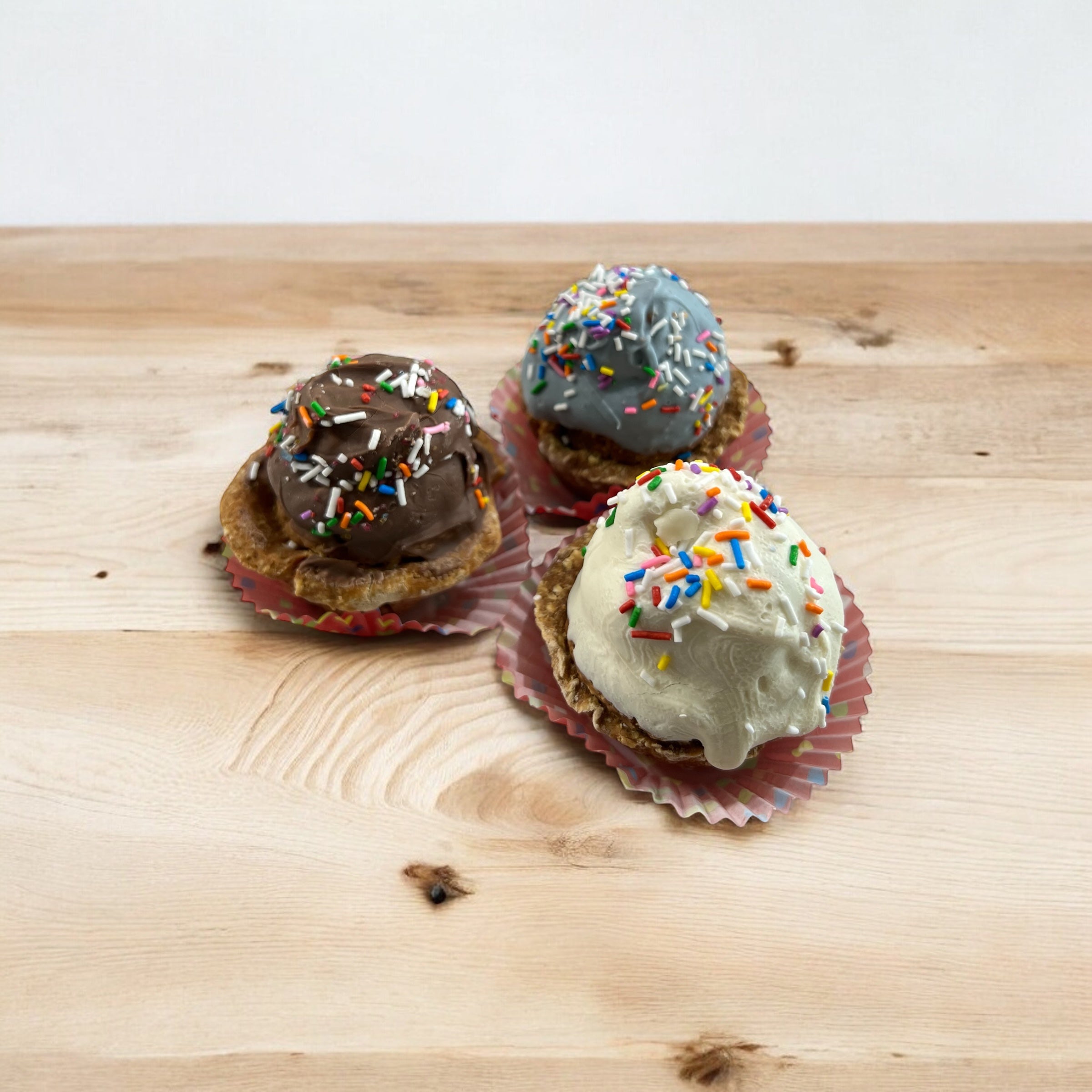 Three dog cupcakes with different toppings and sprinkles on a wooden surface.
