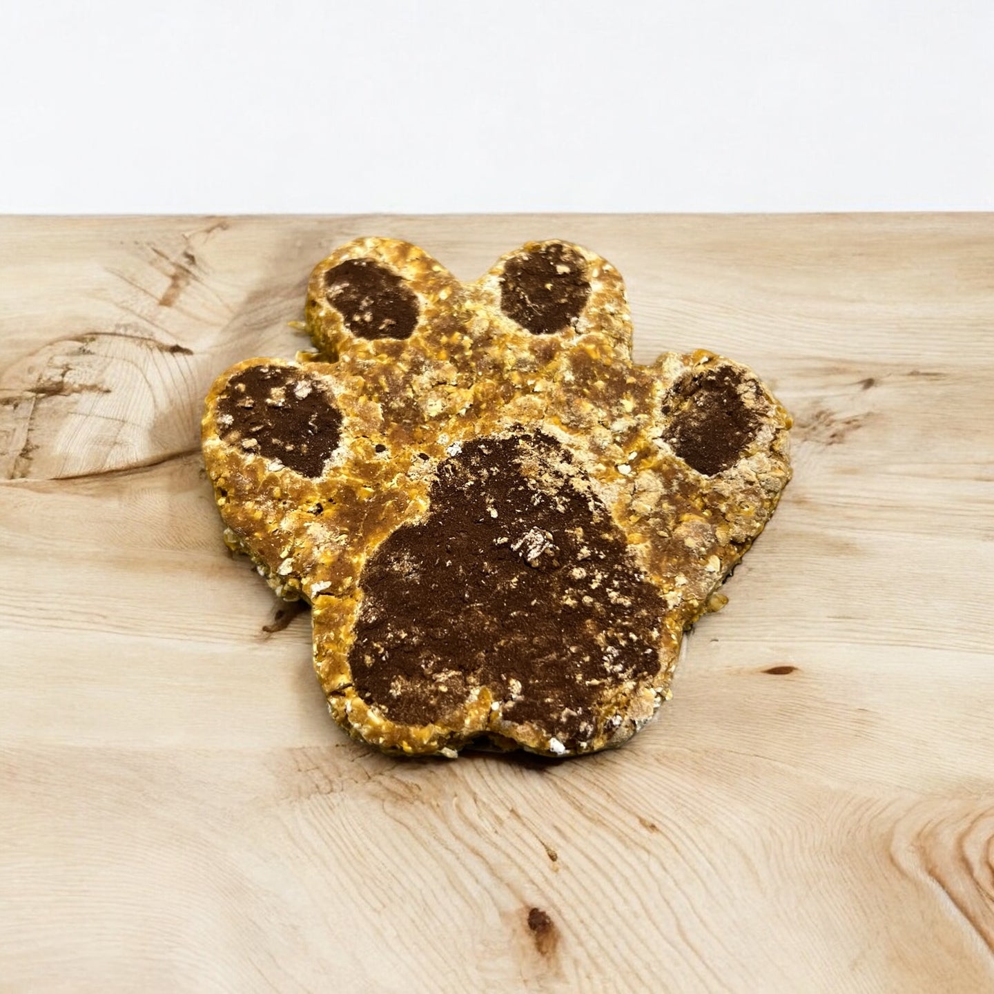 A dog treat shaped like a paw print, displayed on a wooden surface.