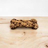 A bone-shaped dog treat with peanut butter and carob drizzled on top, placed on a wooden surface.