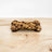 A bone-shaped dog treat with peanut butter and carob drizzled on top, placed on a wooden surface.