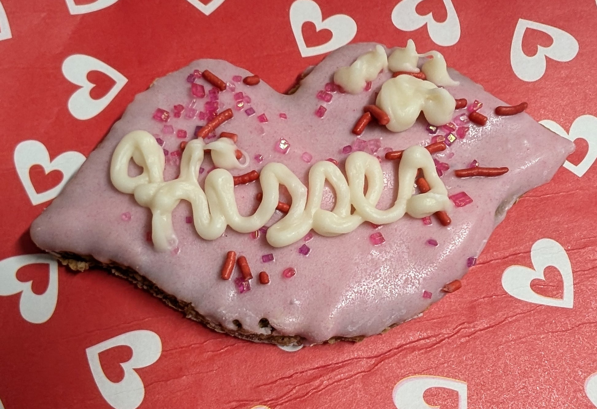 Dog cookie dipped in pink yogurt, with the word kisses piped on.