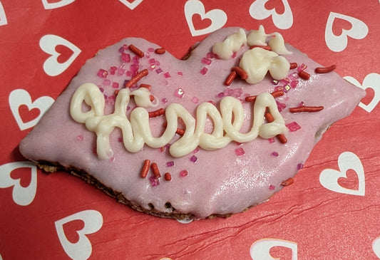 Dog cookie dipped in pink yogurt, with the word kisses piped on.
