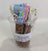 A clear plastic cup containing dog treats. The treats are dipped in various coatings, such as blue and white icing, and are sprinkled with colorful toppings.