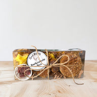A dog treat barkcuterie box containing various natural dog treats such as 'crackers', 'cheese' diamonds, freeze dried strawberries and a squirrel shaped treat, displayed on a wooden surface.