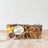 A dog treat barkcuterie box containing various natural dog treats such as 'crackers', 'cheese' diamonds, freeze dried strawberries and a squirrel shaped treat, displayed on a wooden surface.