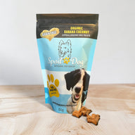 A package of Spoil the Dog brand organic grain-free banana and coconut dog treats. The package is blue and white with an image of a dog and the treats visible in front.