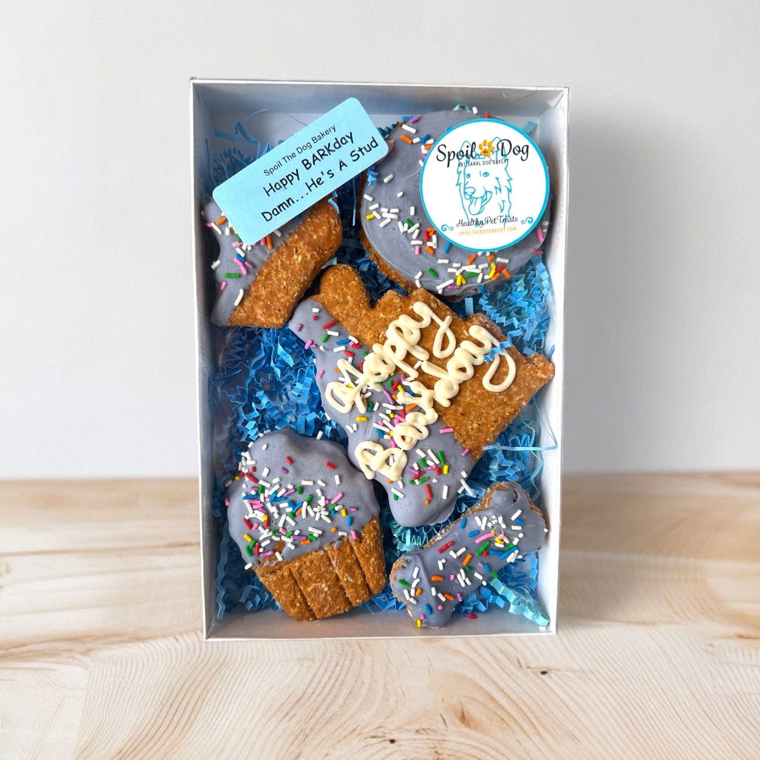 A packaged set of dog treats shaped like birthday cake and bones, decorated with yogurt and sprinkles, with a 'Happy BARKday' label.