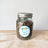 A glass jar filled with carob chips dog treats, labeled with 'Spoil the Dog Bakery' on a wooden surface.