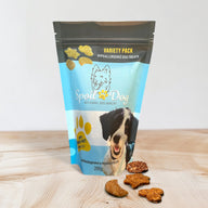 A variety pack of wheat-free dog treats with four different flavors displayed in front of a bag with a dog image and product information.