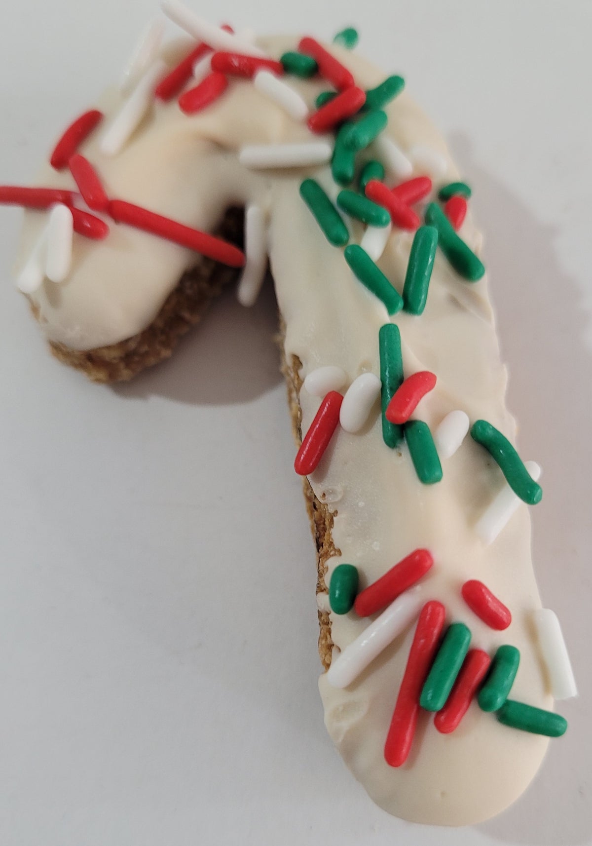 A peanut butter candy cane-shaped dog treat with chickpea flour, oats, peanut butter, yogurt, and sprinkles, decorated with red and green sprinkles on a white background.