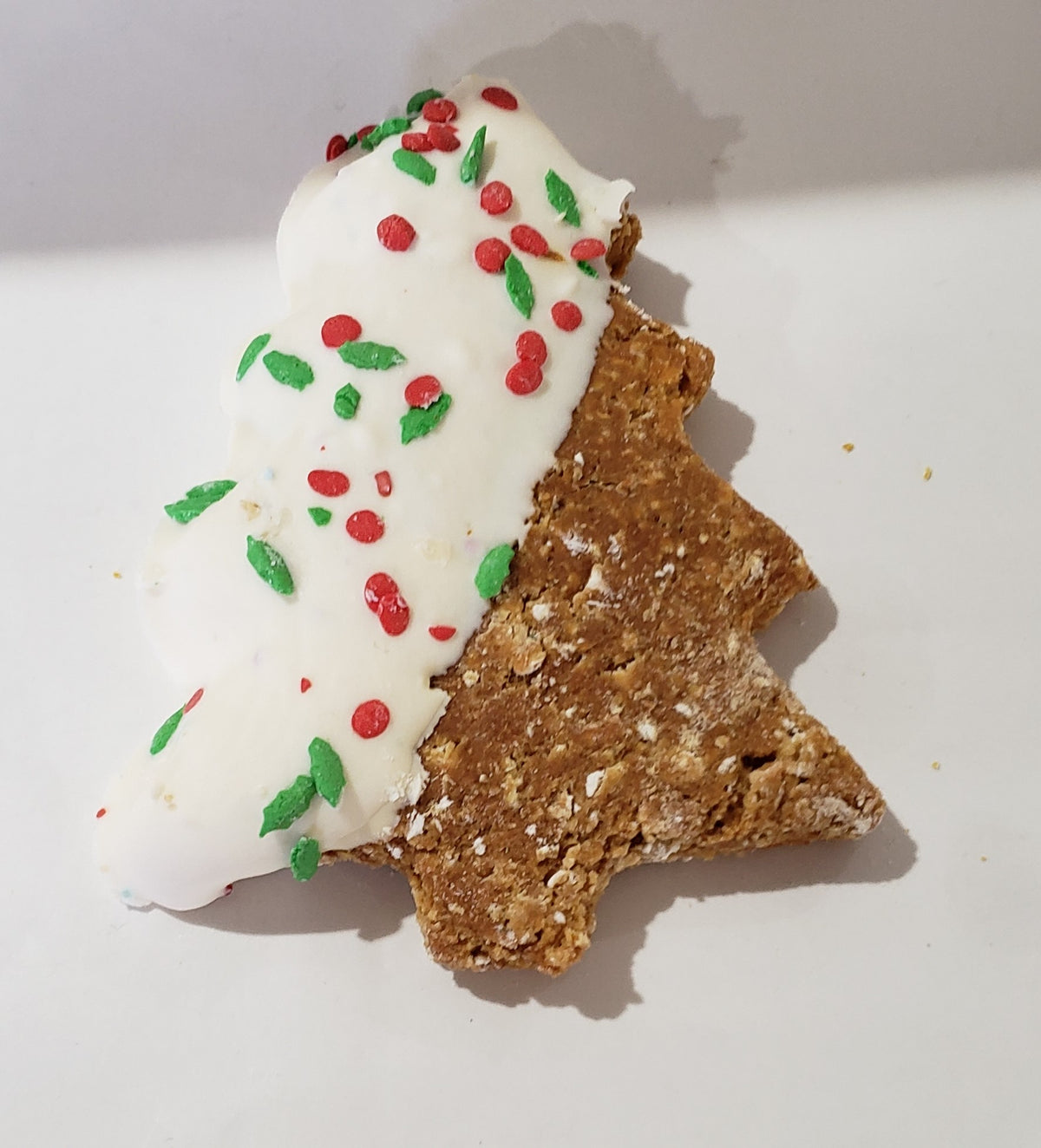 Tree shaped dog cookie half dipped in white yogurt, with sprinkles.