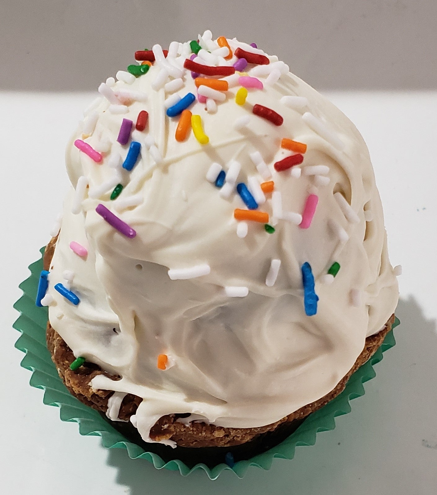 White dog cupcake with sprinkles on a wooden surface.