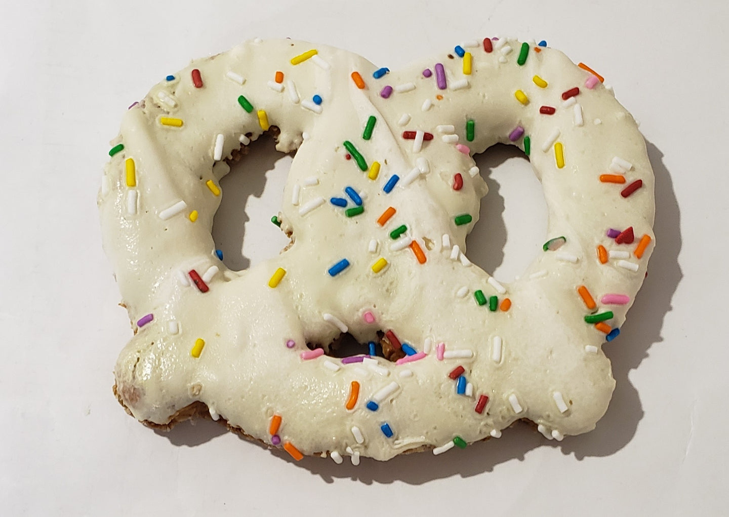 A pretzel-shaped dog treat made with peanut butter and decorated with yogurt or carob, placed on a wooden surface.