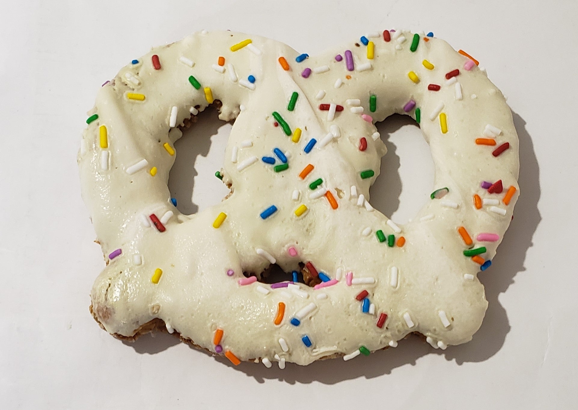 A pretzel-shaped dog treat made with peanut butter and decorated with yogurt or carob, placed on a wooden surface.