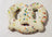 A pretzel-shaped dog treat made with peanut butter and decorated with yogurt or carob, placed on a wooden surface.