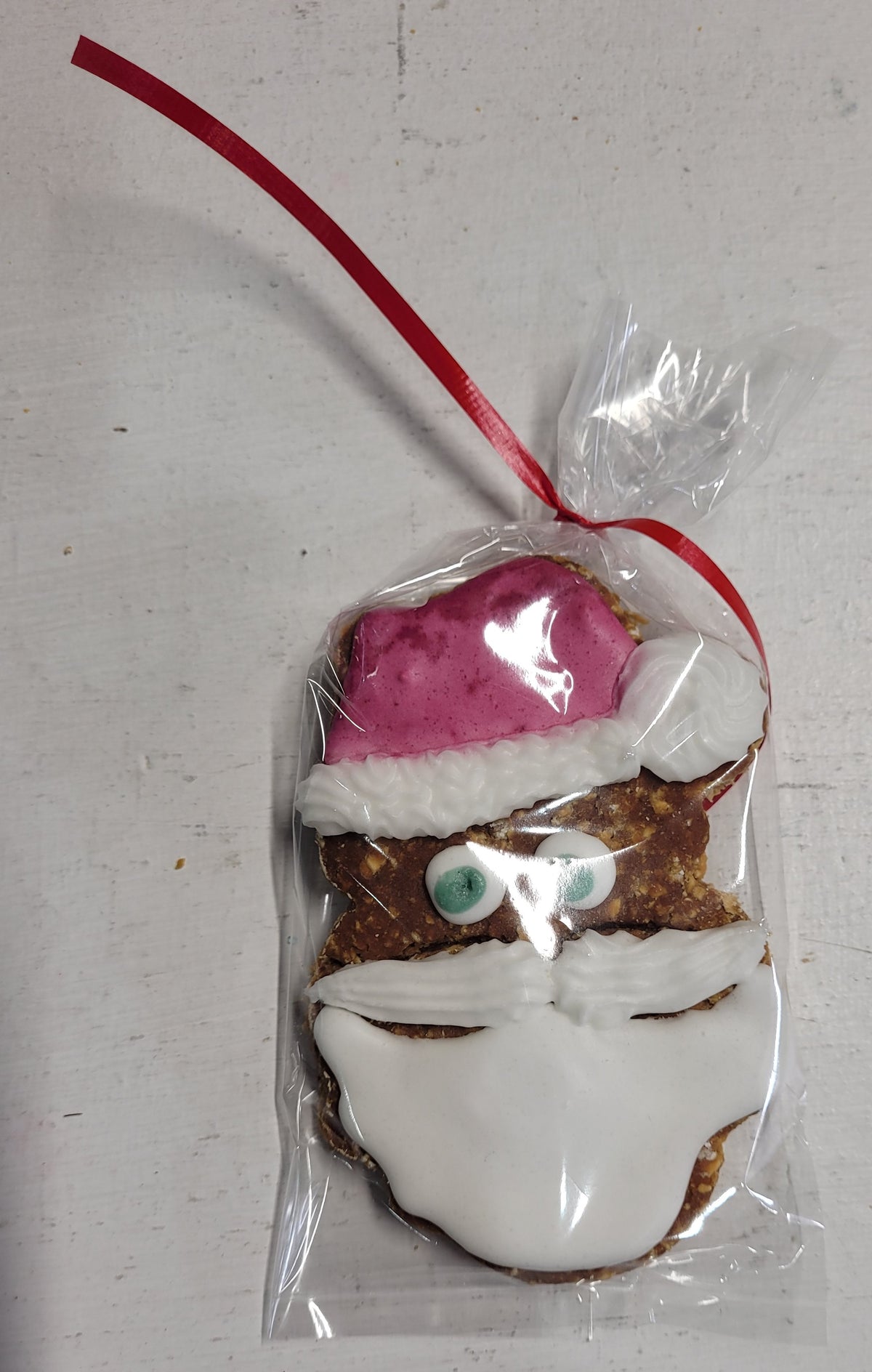 A peanut butter dog treat shaped like a Santa Claus figure, packaged in a clear plastic bag.