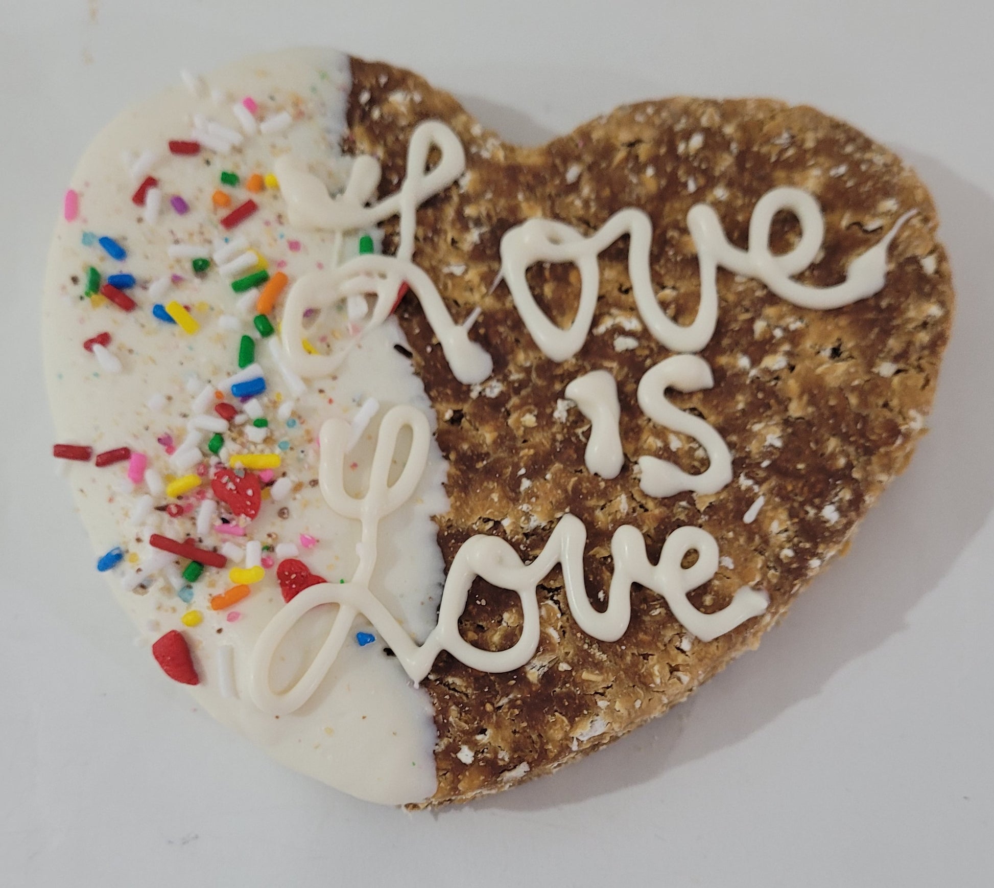 Heart shaped cookie dipped in white yogurt with rainbow sprinkles, with the words "Love is Love" piped in white yogurt.