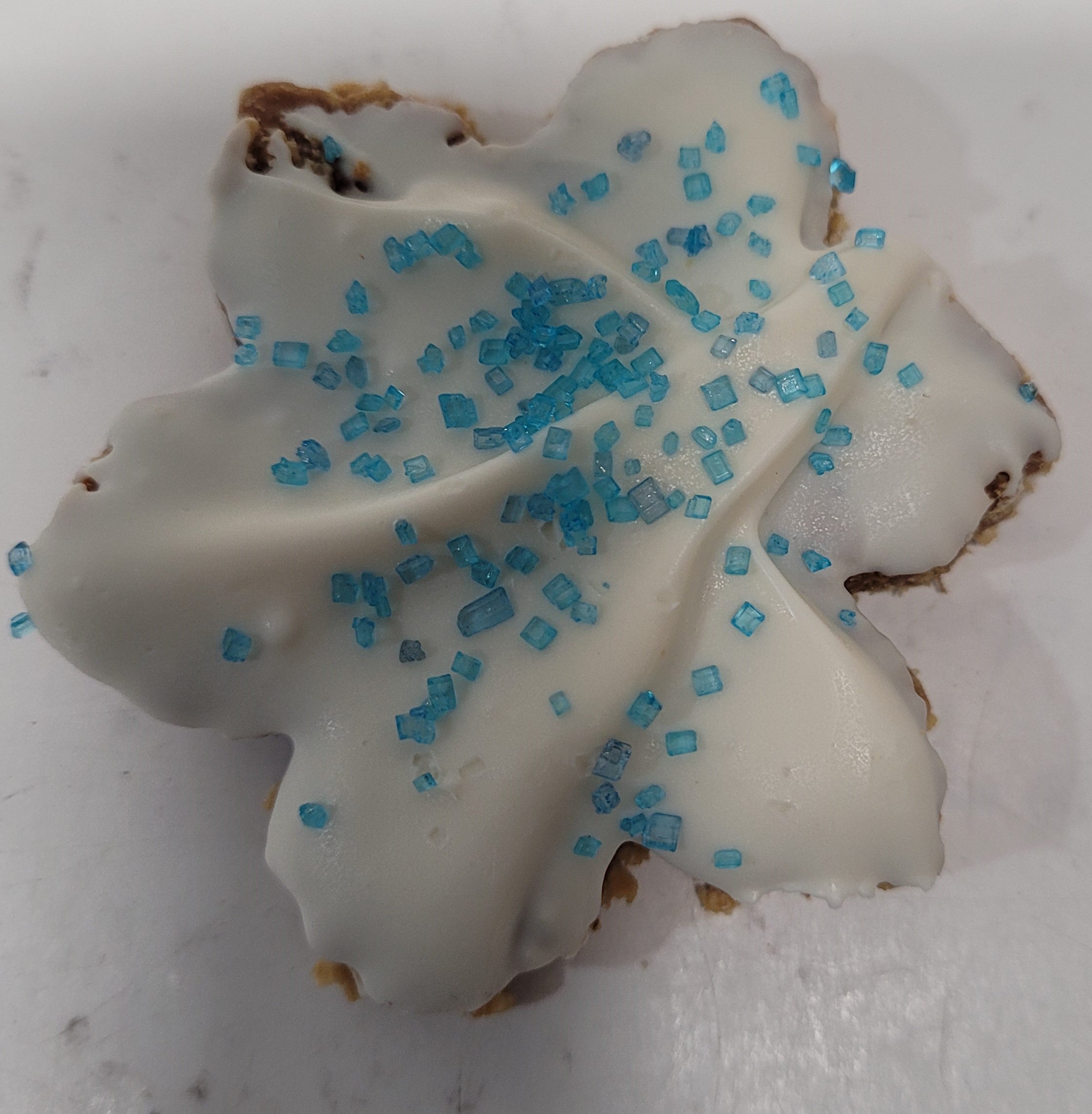 A decorated dog treat shaped like a snowflake with white frosting and blue sprinkles on a white background.