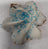 A decorated dog treat shaped like a snowflake with white frosting and blue sprinkles on a white background.